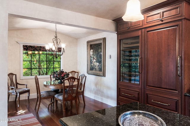 dining area with dark wood-type flooring, an inviting chandelier, and vaulted ceiling