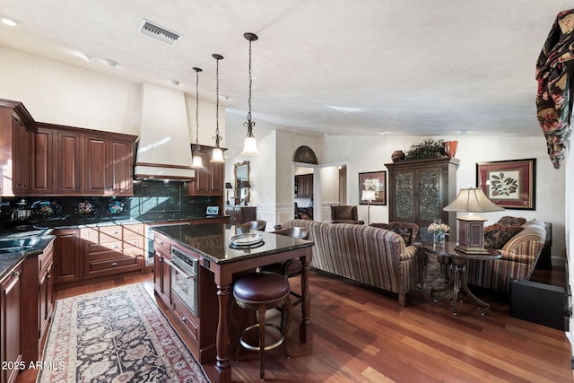 kitchen with stainless steel oven, vaulted ceiling, backsplash, premium range hood, and a kitchen island