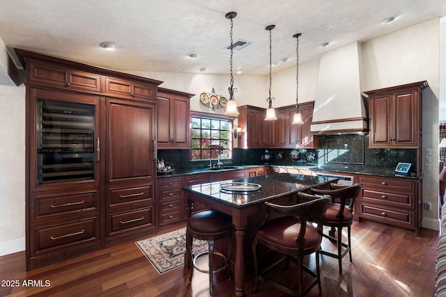 kitchen with custom exhaust hood, pendant lighting, a kitchen island, dark hardwood / wood-style flooring, and dark stone countertops