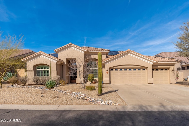 mediterranean / spanish house with a tile roof, stucco siding, roof mounted solar panels, a garage, and driveway