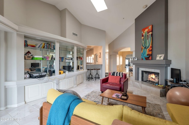 living room featuring high vaulted ceiling, a skylight, and a tile fireplace