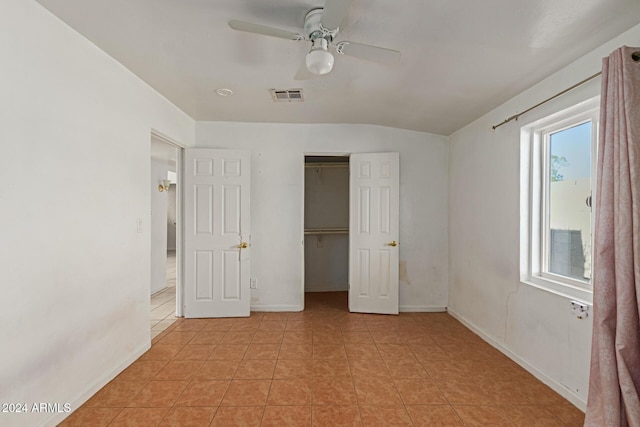 unfurnished bedroom with ceiling fan, a walk in closet, light tile patterned floors, and a closet