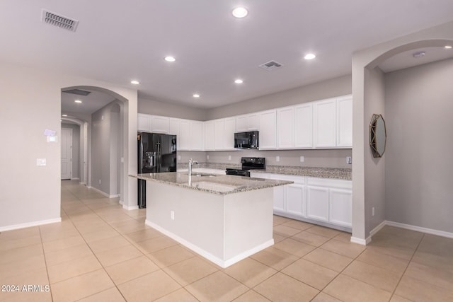 kitchen featuring a center island with sink, black appliances, white cabinetry, light stone countertops, and light tile patterned floors