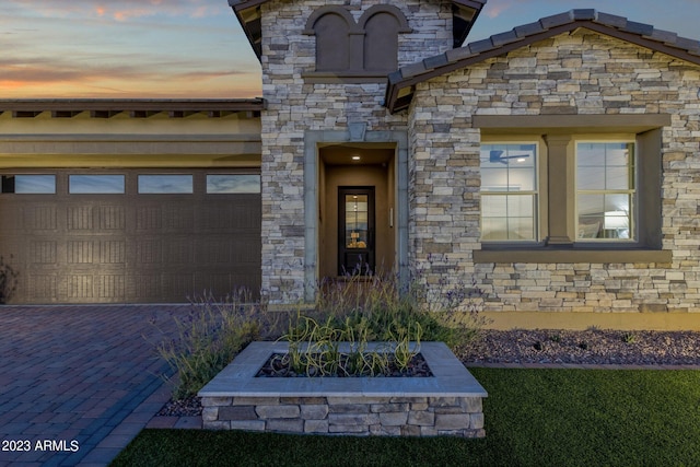 doorway to property featuring a garage, stone siding, and driveway