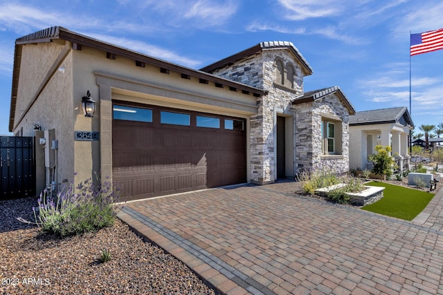 view of front of home with decorative driveway, stone siding, an attached garage, and stucco siding