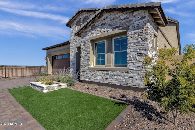 view of side of home with a yard, stone siding, an attached garage, and fence