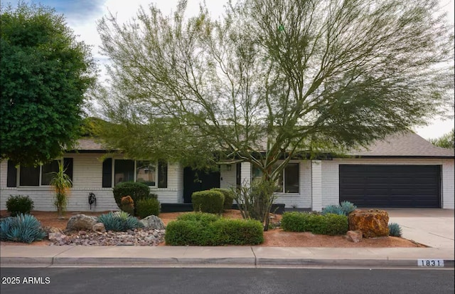 view of property hidden behind natural elements featuring concrete driveway, an attached garage, and brick siding