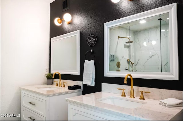 full bathroom with a marble finish shower, two vanities, and a textured wall