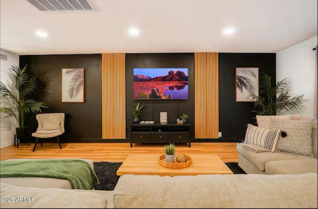 living room with wood finished floors, an accent wall, and recessed lighting