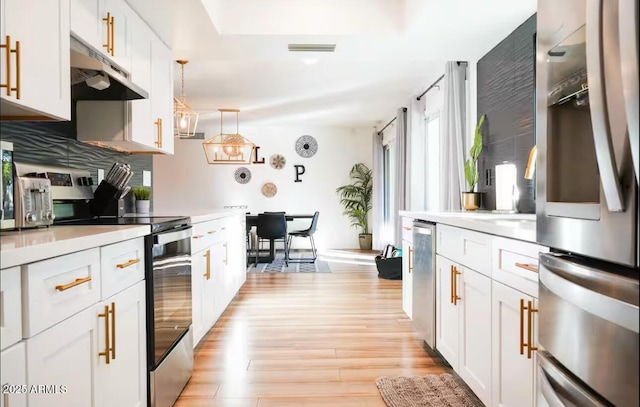 kitchen with appliances with stainless steel finishes, under cabinet range hood, light wood-style floors, light countertops, and white cabinetry