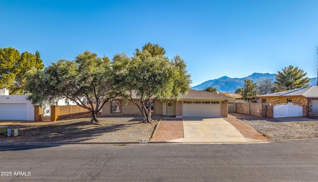 single story home with a gate, driveway, a mountain view, an attached garage, and brick siding