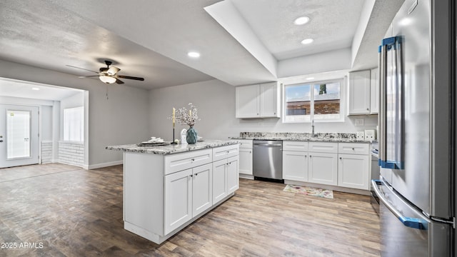 kitchen with light stone counters, light wood finished floors, appliances with stainless steel finishes, white cabinetry, and a center island