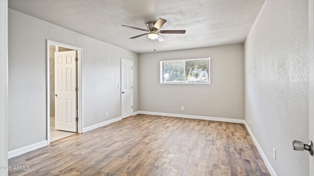 unfurnished room featuring a textured wall, a ceiling fan, baseboards, and wood finished floors