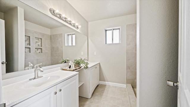 full bathroom featuring tile patterned flooring, a walk in shower, baseboards, two vanities, and a sink