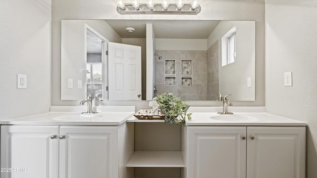 bathroom featuring a sink, tiled shower, and two vanities