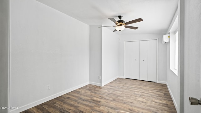 unfurnished bedroom featuring an AC wall unit, wood finished floors, baseboards, and a closet