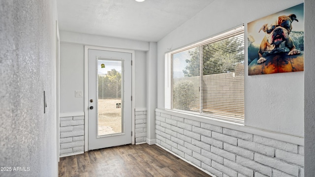 doorway to outside featuring dark wood-type flooring, brick wall, and a textured wall