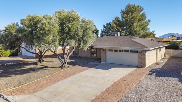 ranch-style home with fence, roof with shingles, concrete driveway, an attached garage, and brick siding