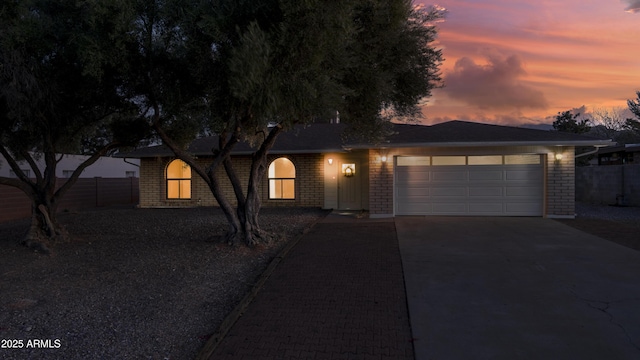 ranch-style home with a garage, brick siding, driveway, and fence