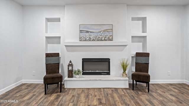 living area with built in features, baseboards, wood finished floors, and a glass covered fireplace