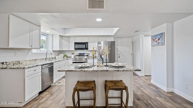 kitchen featuring a tray ceiling, appliances with stainless steel finishes, wood finished floors, and visible vents