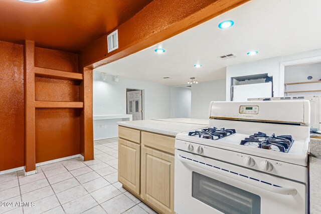 kitchen featuring white range with gas stovetop, light tile patterned floors, and light brown cabinets