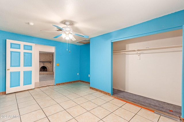 unfurnished bedroom featuring a closet, ceiling fan, light tile patterned floors, and a brick fireplace