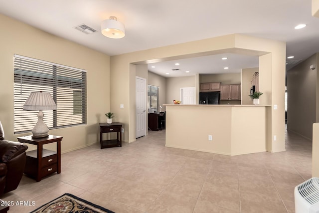 kitchen with light tile patterned floors, black fridge with ice dispenser, and kitchen peninsula