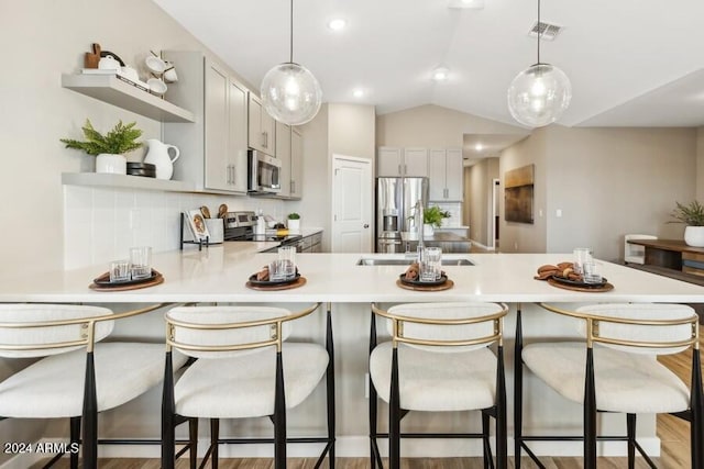 kitchen with kitchen peninsula, a breakfast bar, vaulted ceiling, and appliances with stainless steel finishes