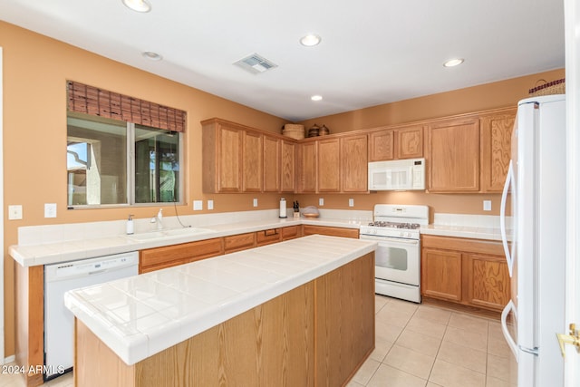 kitchen with white appliances, light tile patterned flooring, sink, a kitchen island, and tile counters