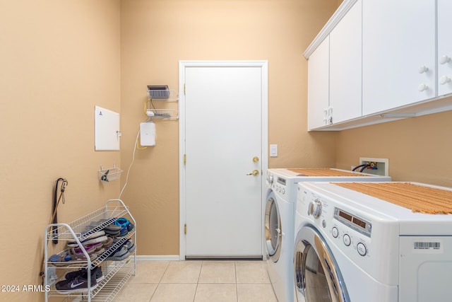 clothes washing area featuring washer and clothes dryer, light tile patterned flooring, and cabinets