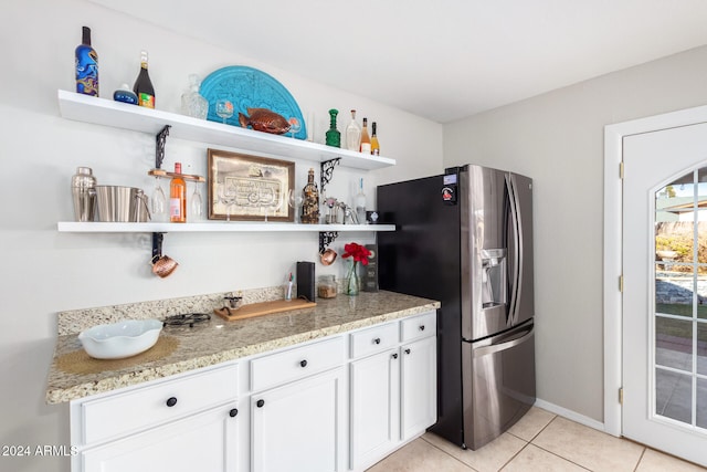 kitchen with light stone countertops, stainless steel fridge, white cabinets, and light tile patterned flooring