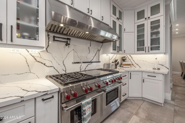 kitchen with light stone countertops, range hood, range with two ovens, decorative backsplash, and white cabinets