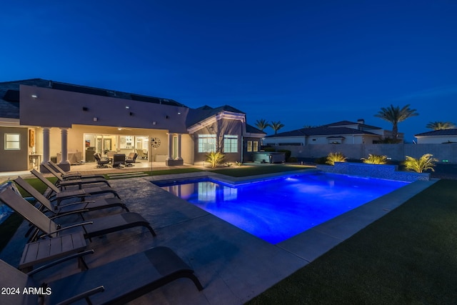 pool at night featuring a patio area