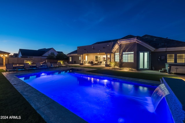 pool at dusk featuring a patio area, pool water feature, and a hot tub