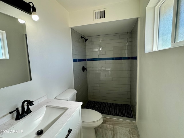 bathroom with a tile shower, toilet, and a healthy amount of sunlight