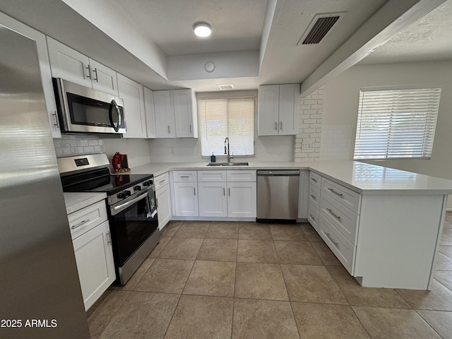 kitchen featuring kitchen peninsula, appliances with stainless steel finishes, a raised ceiling, sink, and white cabinets