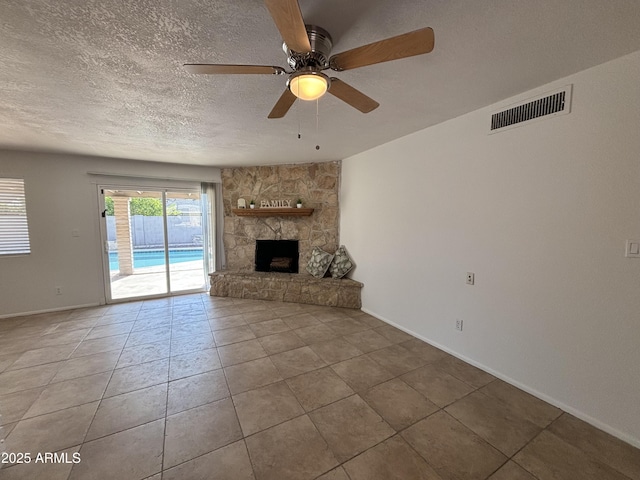 unfurnished living room featuring tile patterned flooring, ceiling fan, a stone fireplace, and a textured ceiling