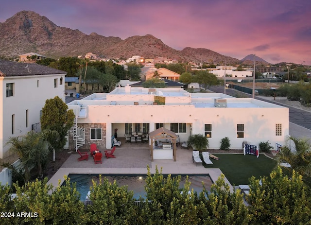 back house at dusk featuring a mountain view, a yard, a patio, and an outdoor living space