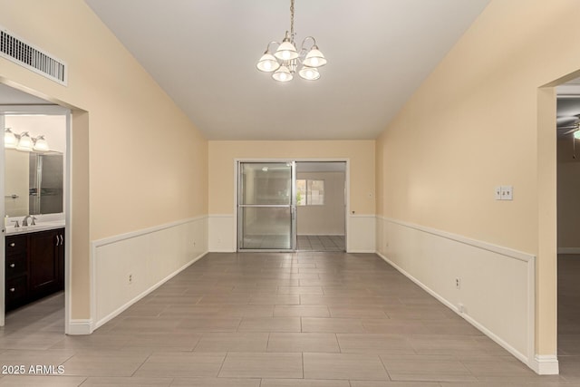 empty room featuring a notable chandelier, visible vents, wood tiled floor, wainscoting, and a sink