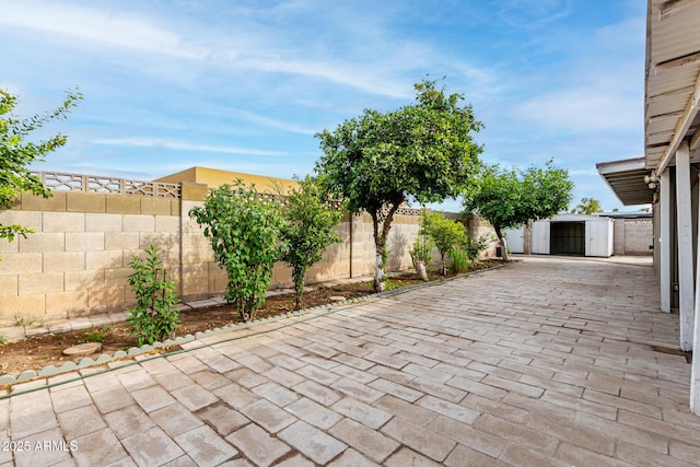 view of patio / terrace featuring a fenced backyard, a storage unit, decorative driveway, and an outdoor structure