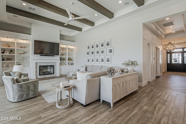 living room featuring a glass covered fireplace, ceiling fan with notable chandelier, wood finished floors, and visible vents