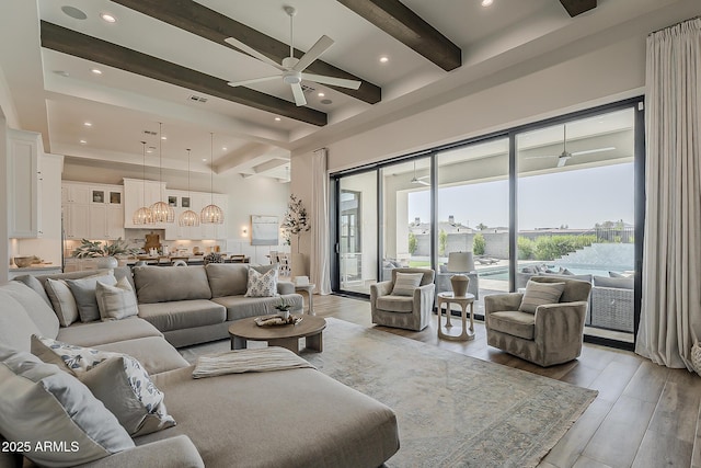 living room with a high ceiling, light wood finished floors, beam ceiling, and ceiling fan with notable chandelier
