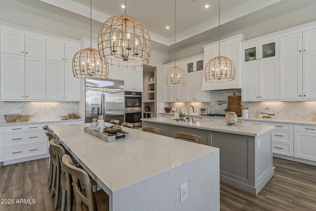 kitchen featuring an inviting chandelier, decorative backsplash, stainless steel appliances, and an island with sink