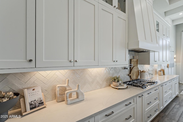 kitchen featuring stainless steel gas stovetop, premium range hood, white cabinets, and glass insert cabinets