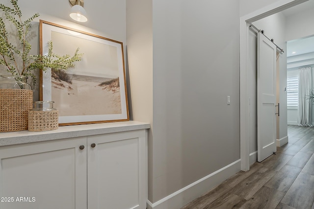 hallway featuring baseboards, a barn door, and wood finished floors