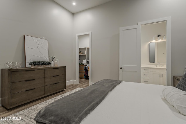 bedroom featuring connected bathroom, a walk in closet, a sink, wood finished floors, and a closet