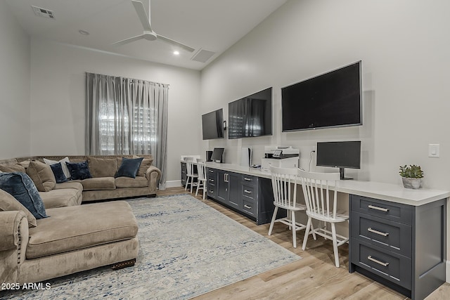 living room with built in study area, ceiling fan, light wood finished floors, and visible vents
