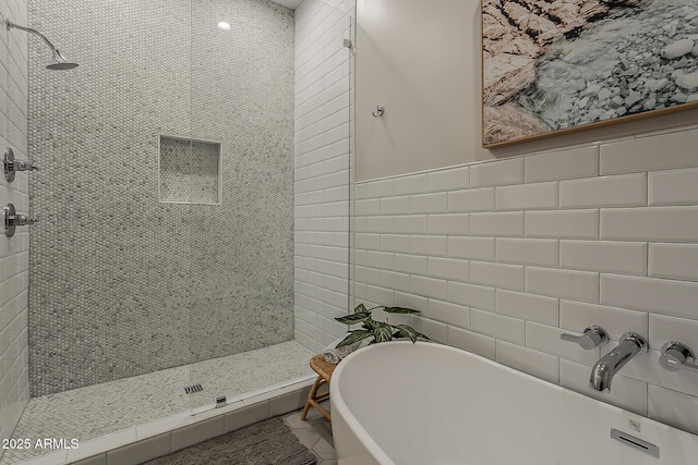 bathroom featuring tile walls, a freestanding tub, tiled shower, and a sink