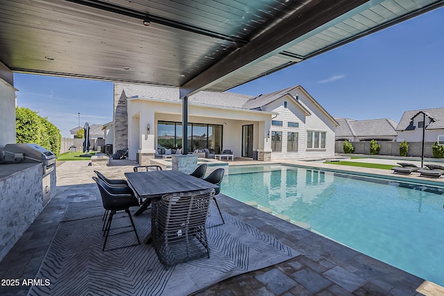 view of swimming pool featuring a patio area, a fenced in pool, a fenced backyard, an outdoor kitchen, and a grill